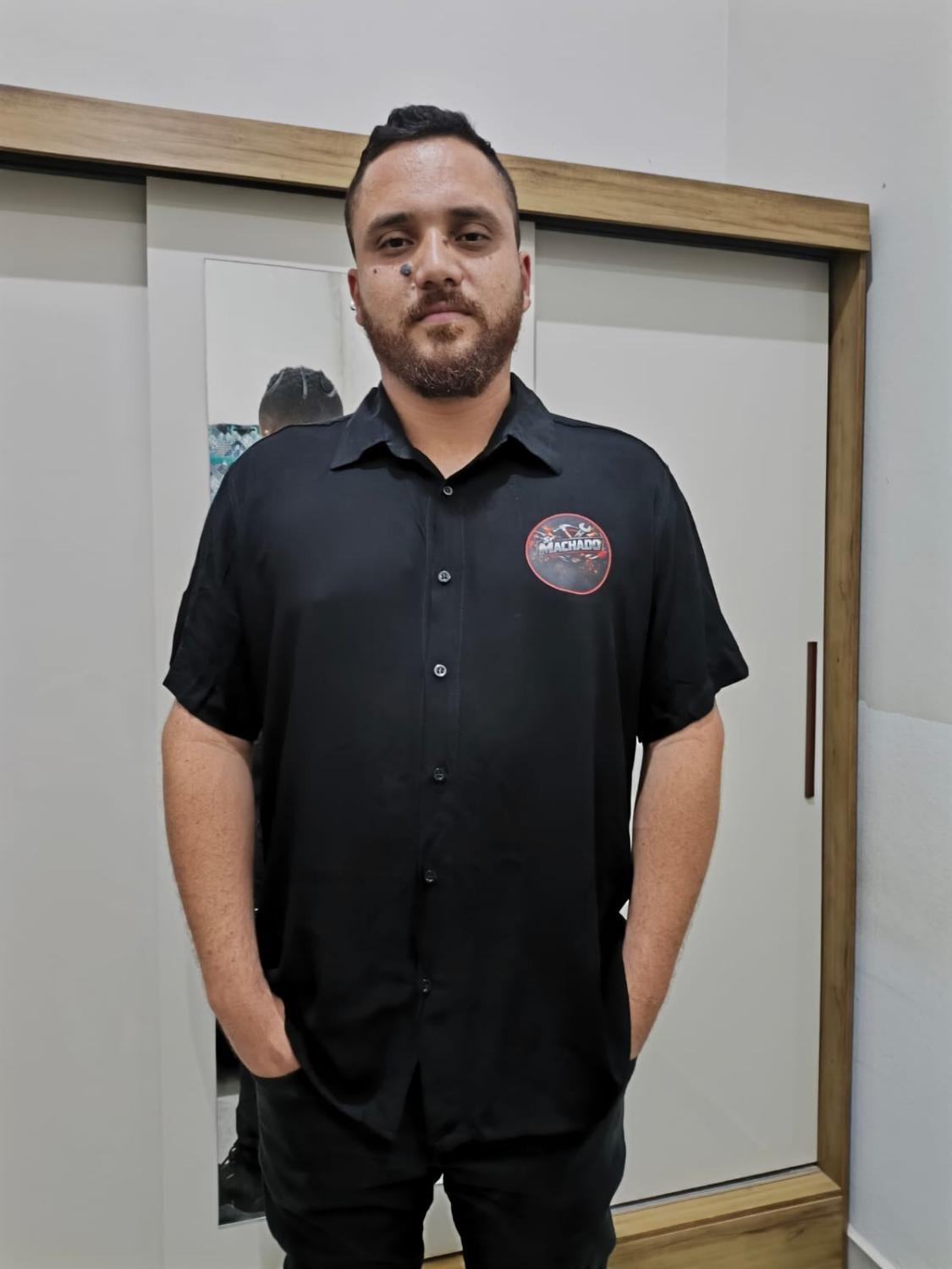 Machado, montador de móveis, de camisa preta com o logo Machado, em pose profissional